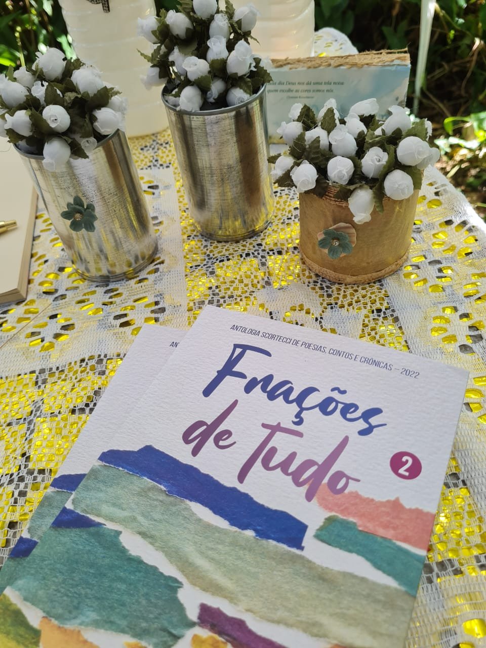 Livros de poesia e pequenos arranjos artesanais em uma mesa no jardim