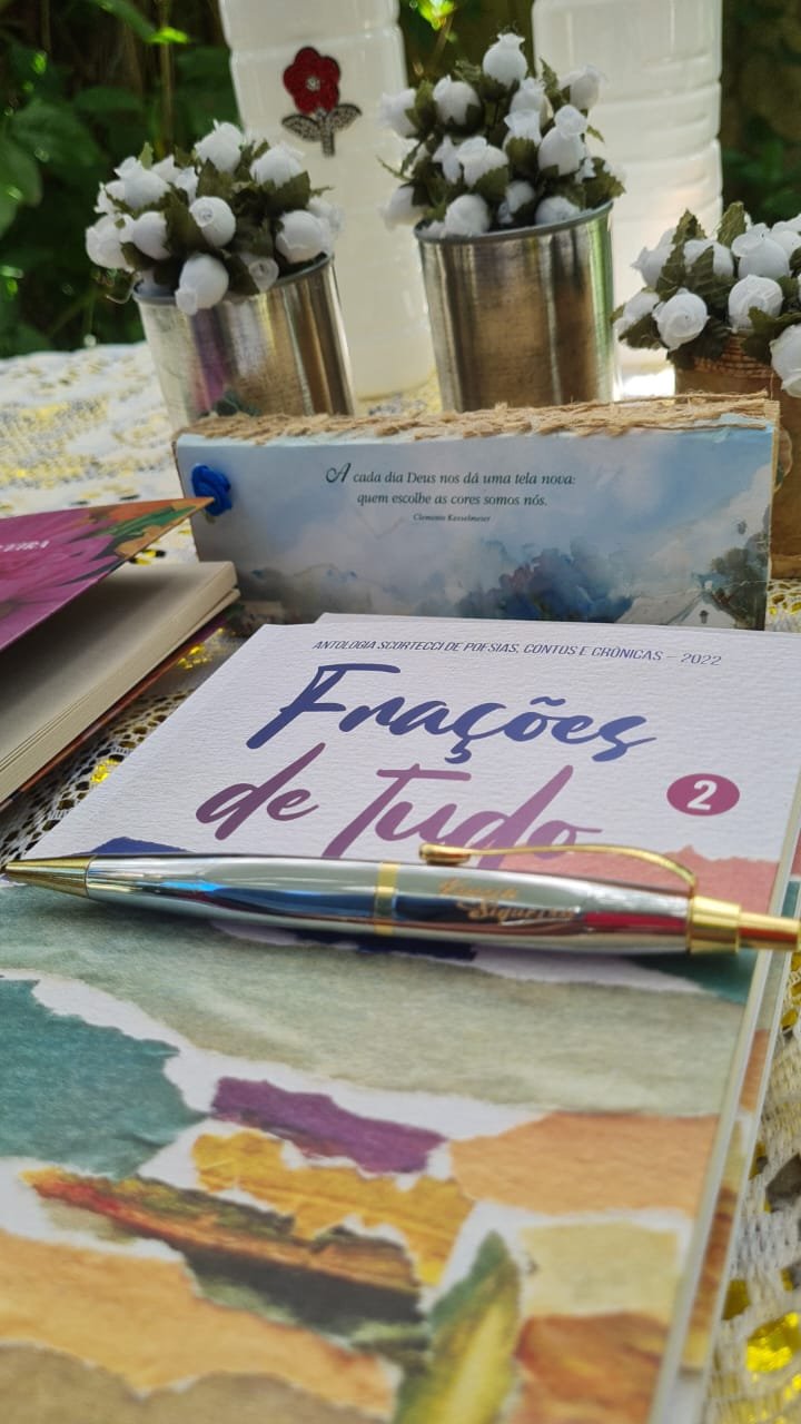 Livro de poesia, caneta e arranjos artesanais sobre uma mesa